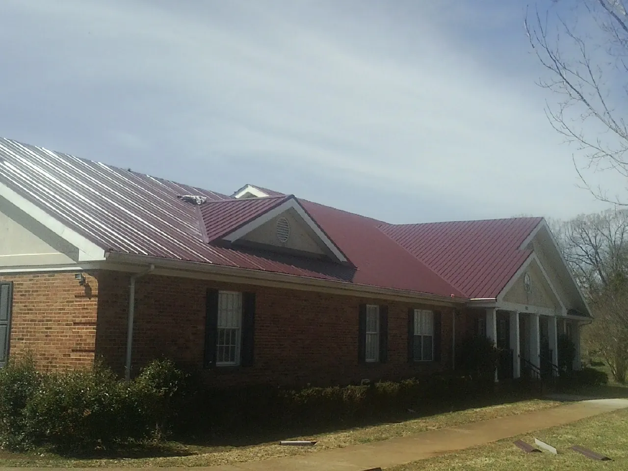 Red metal roof with gabled entries on a long brick building, from a Hail Damage Roof Repair job in Cayuta