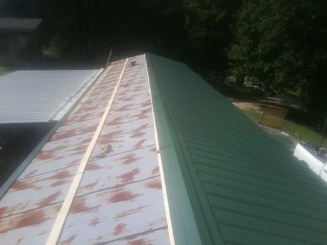 Old rusted panels beside newly installed green metal roofing — Wind Damage Roof Repair by Roofing Brothers in Cayuta