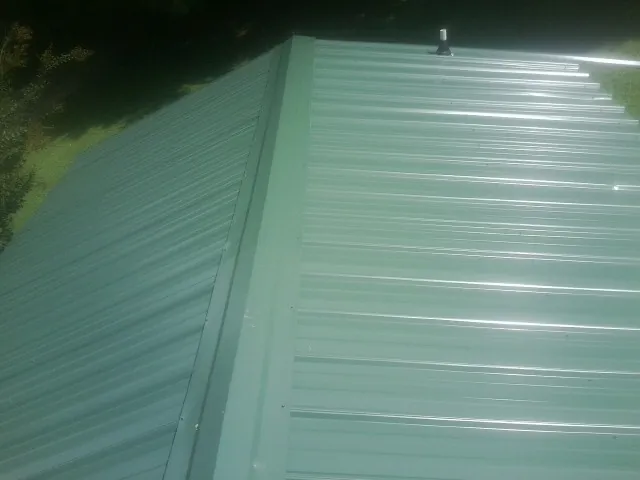 New green metal panels meeting at the ridge of a roof — Flat Roof Repair work by our crew in Cayuta