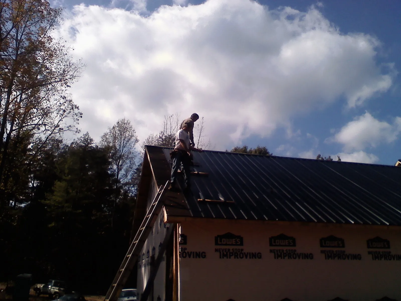 Roofer fastening dark metal panels high against a cloudy sky, from a Roof Inspection job in Cayuta