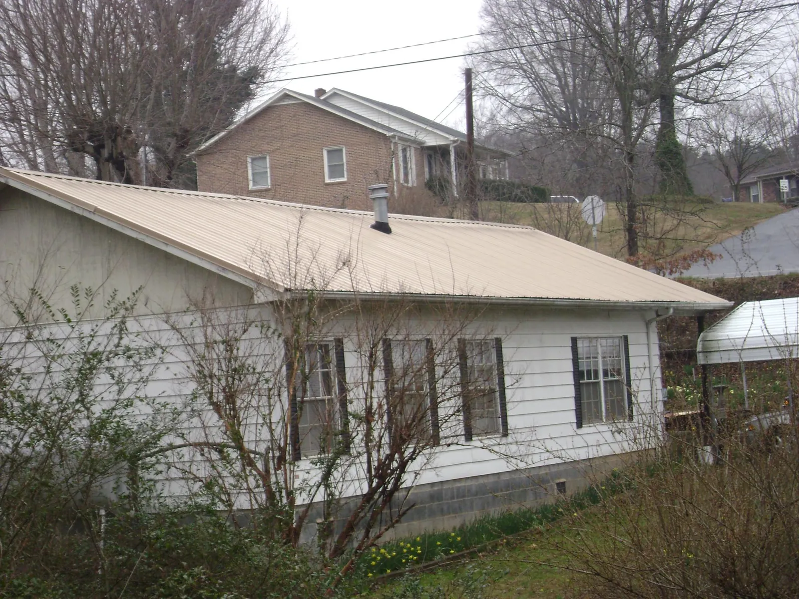 Tan metal roof on a white sided house set into a hillside — Commercial Roofing by Roofing Brothers in Cayuta