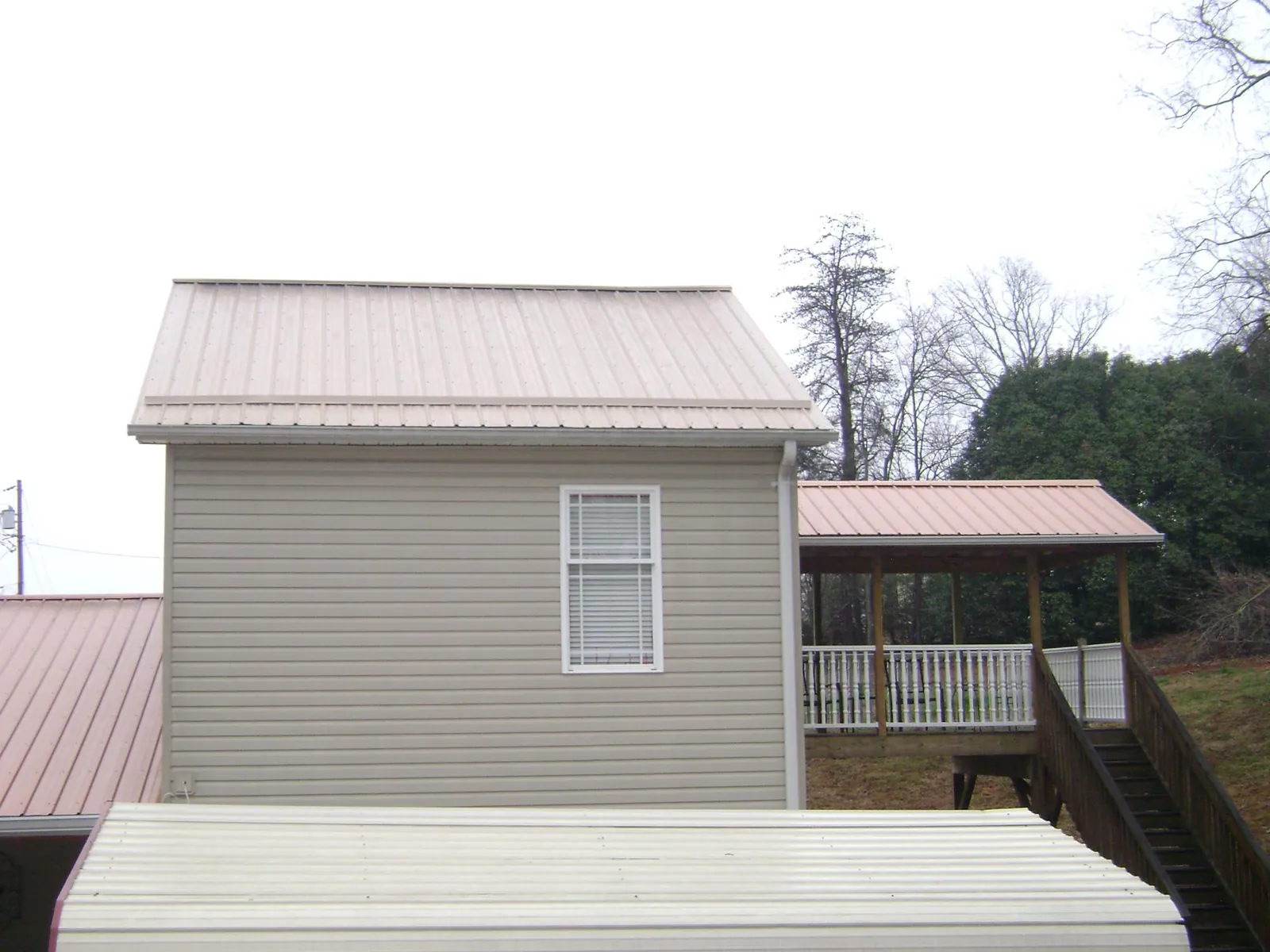 Tan metal roofs on a two story addition and attached porch, from a Roof Replacement job in Cayuta